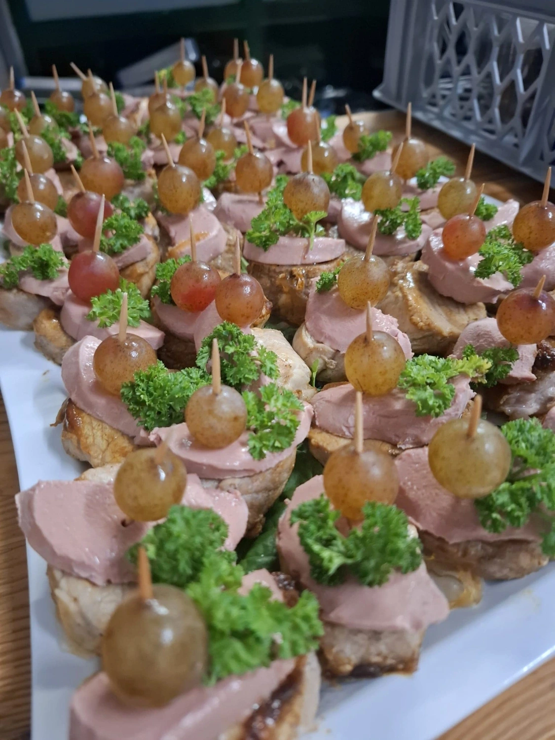Canapés mit Leberpastete, Weintraube und Petersilie auf gerösteten Baguettescheiben, dicht in Reihen angerichtet