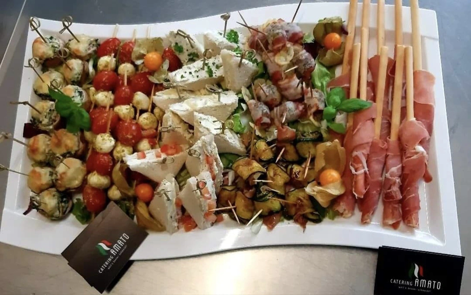 Große gemischte Fingerfood-Platte mit Mini-Quiches, Caprese-Spießen und Zucchini-Röllchen auf einer Edelstahltheke
